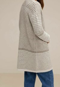 Světle šedý kardigan s texturovaným vzorem, se žebrovaným detailem na límci a manžetách, v kombinaci s modrými denimovými džíny.