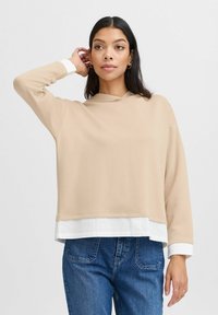 Beige hoodie met lange mouwen, met een witte shirtzoomdetail aan de onderkant. Zacht materiaal, ontspannen pasvorm.
