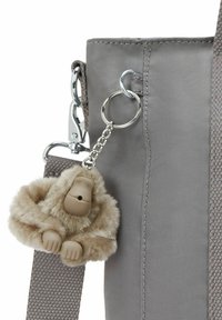 Borsa di stoffa grigia con un portachiavi a forma di scimmia di peluche attaccato tramite una catena argentata. Il portachiavi presenta pelo morbido e mani simili alla gomma.