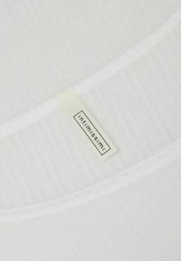 White ribbed fabric with a smooth texture. Features a sewn label with the brand name "intimissimi" in a rectangular black outline.