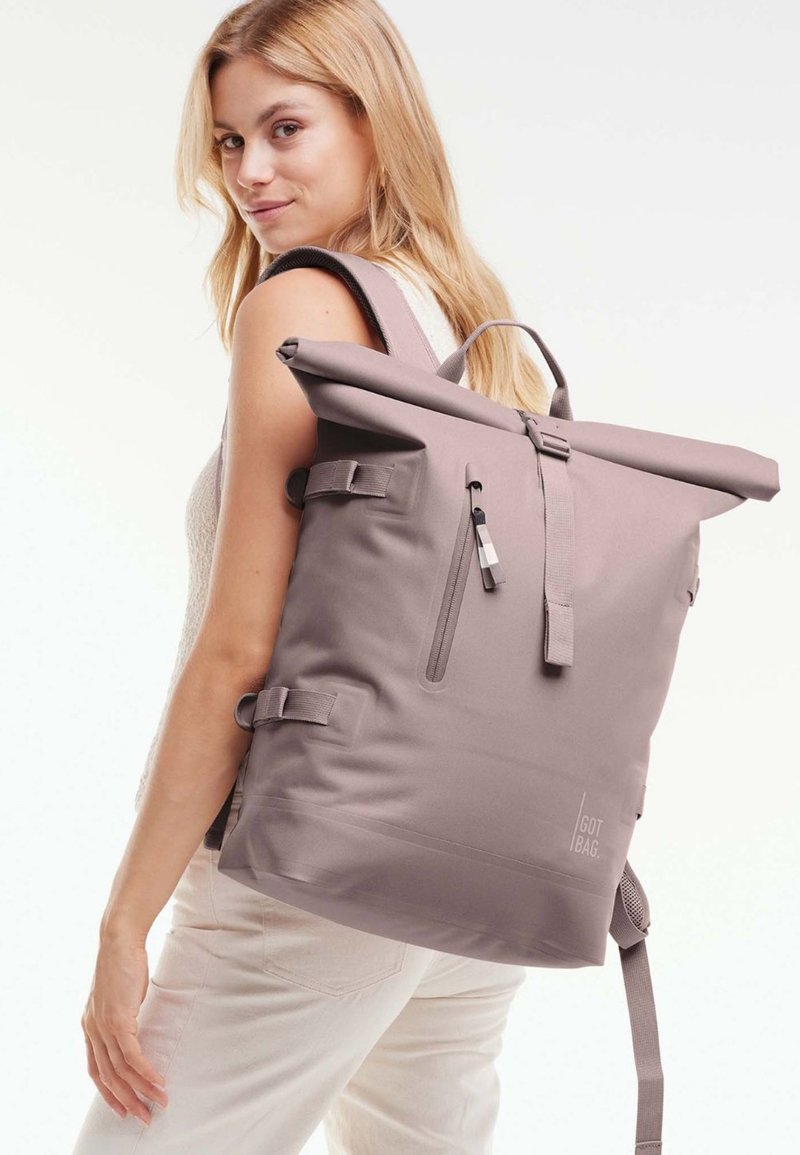 Rucksack mit Rollverschluss aus weichem Taubengrau-Material; ausgestattet mit Reißverschlüssen, verstellbaren Riemen und seitlichen Schnallen für einen sicheren Verschluss. Mit strukturierter Oberfläche.