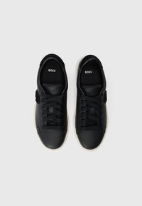 Sneakers in pelle nera con finitura testurizzata, punta rotonda e lacci piatti. Presentano un dettaglio del logo sulla linguetta e una suola in gomma a contrasto.