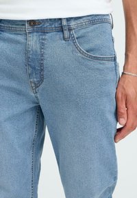 Gai zila džinsu bikses ar taisnu piegriezumu, kurām ir viegla vīšana, izšūts dekors un viens pogas aizdare ar rāvējslēdzēju. 