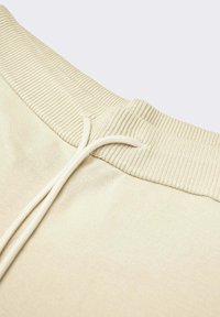 Pantalones de chándal de algodón beige con cintura acanalada, cierre de cordón y textura suave. Presenta un diseño sencillo y sin costuras.