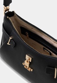 Czarna torebka ze skóry o fakturze, z zapięciem logo w kolorze złotym, zamkiem błyskawicznym oraz beżowym wnętrzem wyposażonym w przegródki na karty i kieszeń na zamek.