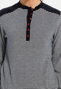 Randig långärmad skjorta med marinblå och vita horisontella ränder, en knäppt hals och röda knappar på knappslån. Mjuk textur.