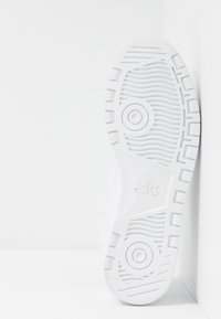 Bílá podrážka tenisky s texturovaným vzorem, kruhovým detailem na střední části podrážky a značením. Plochý, široký design pro lepší přilnavost, s vyvýšenými drážkami pro trakci.
