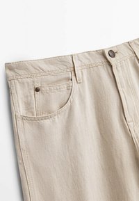 Beige farkkutakit suoralla lahkeella, jossa on yksi etutasku, metallinapit ja näkyvät ompeluyksityiskohdat.