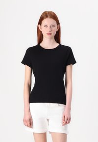 T-shirt nera a maniche corte con scollatura rotonda, realizzata in morbido tessuto di cotone, design aderente, indossata con pantaloni corti bianchi con orlo arrotolato.