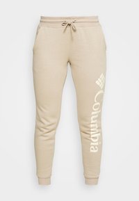 Beige sweatpants gjorda av mjukt tyg, med en tapered design, elastisk midja med dragsko, och Columbia-logotyp i ljus färg på sidan.