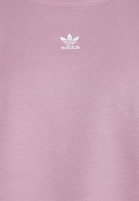 Rosa bomullströja med rundad halsringning och en vit Adidas-logotyp på bröstet. Tyget har en slät, texturerad yta.