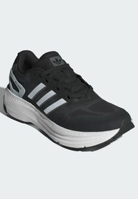 Zapatilla deportiva negra con detalles en blanco y gris. Presenta una parte superior de malla texturizada, cierre de cordones, suela acolchada y el logo de tres rayas.