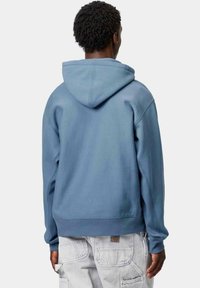 Sudadera de algodón azul con un corte relajado, que presenta una capucha con cordón y puños de canalé, mostrada desde atrás sobre un fondo neutro.