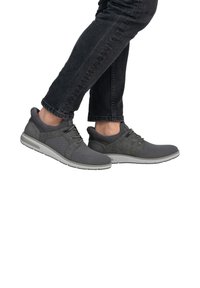 Baskets de sport grises avec tige en maille et en daim, design à lacets et semelle en caoutchouc blanche. Portées avec un jean foncé, montrant le profil et le mouvement.