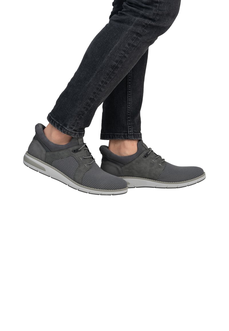 Scarpe da ginnastica grigie con superiore in rete e camoscio, design con lacci e suola in gomma bianca. Indossate con jeans scuri, che mostrano profilo e movimento.