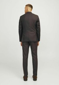 Dunkelgrauer Anzug mit einem strukturierten Blazer und maßgeschneiderten Hosen, gefertigt aus glattem Stoff mit feinen Nähten. Braune Schuhe runden den Look ab.
