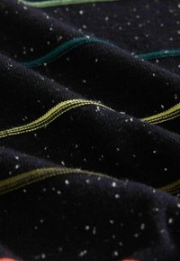 Material textil negru cu stropi multicolori, prezentând dungi ondulate în contraste de verde și galben. Textură moale, cu detalii de cusătură vizibile.