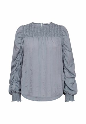 Svetlosivá blúzka s textúrovaným povrchom, zberom pri ramenách a manžetách a uzáverom na chrbte s výrezom. Má vertikálne pruhy.
