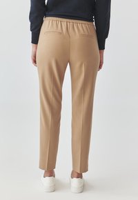 Tan stretchbroeken met een ontspannen pasvorm, voorzien van een elastische tailleband en twee achterzakken, gestyled met witte sneakers.