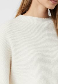 Weißer, gerippter Pullover mit hohem Kragen und strukturierter Stoffoberfläche. Verfügt über eine lockere Passform und weiches, warmes Material.