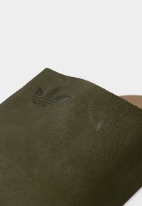 Πράσινο χρώμα ελιάς σατινέ σανδάλι με υφή, με ανάγλυφο λογότυπο στην επάνω επιφάνεια. Μινιμαλιστικός σχεδιασμός, ανοιχτή μύτη.