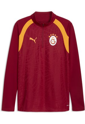 Langærmet mørkerød sportjakke med gule skulderaccenter, lynlås foran, Puma-logo og et Galatasaray fodboldklubemblem med fire stjerner.