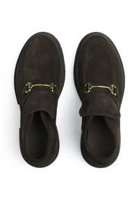 Mocassins en daim marron avec un bout arrondi, des coutures décoratives et un accent métallique vert sur la bride. Semelle en caoutchouc noir mat.
