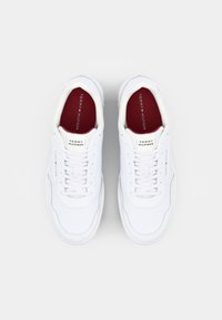 Baskets blanches avec une tige en cuir lisse, dotées d'un bout rond, d'un système de laçage, d'une doublure rouge et du logo "TOMMY HILFIGER" sur la languette.