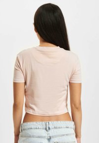 Light pink, short-sleeve crop top with a round neckline; soft fabric with a smooth texture, worn with high-waisted denim shorts.