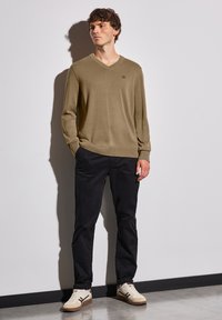 Beige v-ringad tröja med långa ärmar, matchad med svarta byxor och beige sneakers med bruna detaljer. Slät tyg, avslappnad passform.