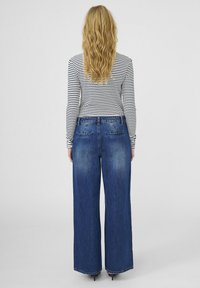 Jeans de mezclilla de pierna ancha en azul medio, con cintura alta, dos bolsillos traseros y un desvanecimiento mínimo. Combinados con una camiseta de manga larga a rayas en blanco y negro.