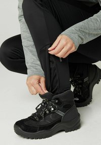 Zwarte wandelbroek met een slank ontwerp en rekbaar materiaal, gecombineerd met zwarte laarzen met vetersluiting en gestructureerde accenten.