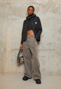 Zwarte gewatteerde jas met een cropped ontwerp, grijze wijde broek en zwarte chunky schoenen. Houdt een handtas met luipaardprint vast.