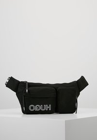 Marsupio in tessuto nero con una superficie liscia, dotato di un vano principale con zip e di una tasca frontale più piccola. Accentuato da un logo bianco.