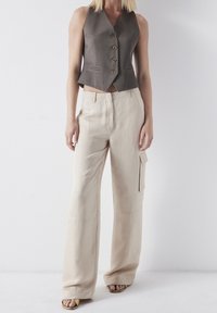 Brązowa bez rękawów kamizelka z pięcioma guzikami, w połączeniu z beżowymi spodniami cargo o szerokich nogawkach, z bocznymi kieszeniami i gładką fakturą.