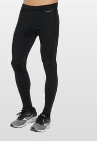 Zwarte sportleggings gemaakt van flexibel materiaal, met een strakke pasvorm en subtiele stikdetails. Gecombineerd met sportieve schoenen.