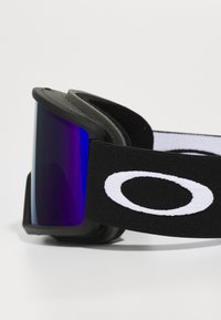 Gogle narciarskie z zakrzywionym fioletowym szkłem, czarną gumową ramą i czarnym paskiem z wyraźnym białym okrągłym logo.