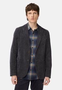 Donkergrijze blazer van zachte stof met een relaxte pasvorm, twee voorzakken en een sluiting met twee knopen over een blauw geruit overhemd.