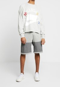 Ljusgrå sweatshirt med färgglogt Nike-logotyp och text. Svart och vit rutigt shorts med vikta fållar. Vita sneakers.