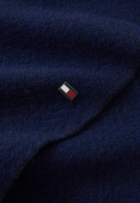 Mørkeblå uldstof med et herringbone mønster, prydet med en lille rektangulær nål i sort, hvid og rød.