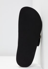 Semelle de chaussure noire avec une surface texturée et nervurée; forme de bout arrondi; design minimaliste sans marque ni ornements visibles.