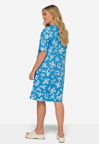 Vestido azul de manga corta con un patrón de coral blanco. De media longitud, con un ajuste relajado y tejido suave. Combinado con sandalias de plataforma de color claro.