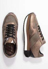 Sneakers made of bronze fabric with mesh panels, a textured surface, black laces, a brown accent stripe, and a rubber sole.