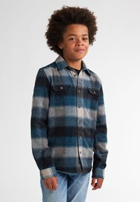 Camisa de franela en estampado de cuadros azul, negro y gris. Cuenta con un cuello, botones al frente y dos bolsillos en el pecho. Textura suave, mangas largas.