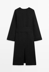 Robe midi noire à manches longues avec larges manches, panneau de taille ajusté et fente centrale au dos, présentée à plat sur fond blanc.