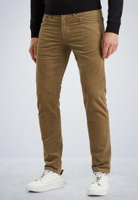 Pantalones de pana marrón con un ajuste slim, bolsillos delanteros y una textura suave, combinados con zapatillas blancas.