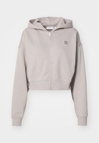 Hoodie court en gris clair, fabriqué à partir d'un tissu doux. Il présente une fermeture éclair sur le devant, une capuche ajustable et un logo brodé sur la poitrine.