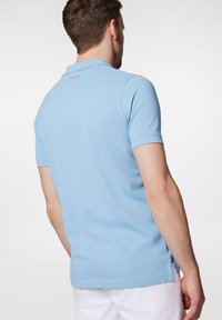 Jasnoniebieska koszulka polo z przepuszczającego powietrza materiału, z klasycznym kołnierzykiem i krótkimi rękawami. Szczegół z logo w kolorze czerwonym z tyłu.