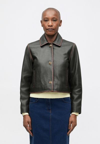 Veste en cuir noire cropped avec un col, des boutons dorés et des surpiqûres claires contrastantes. Associée à un pull vert clair et une jupe en denim.