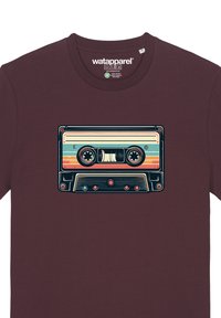 T-shirt bordeaux avec un graphique de cassette rétro coloré. Le design présente des rayures horizontales, des bobines circulaires et des boutons dans des couleurs claires.